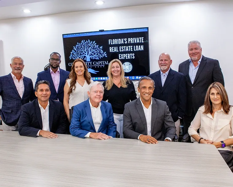 Ten business professionals posed around a conference table in a modern office; screen behind reads 'Florida's Private Real Estate Loan Experts'.